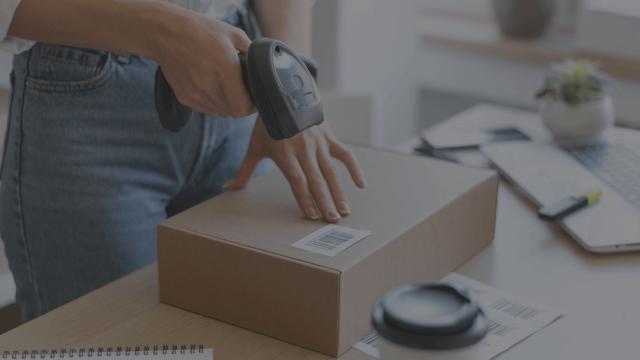 A woman scanning a package on the desk with a barcode scanner